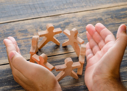 Business success concept on wooden background high angle view. hands protecting wooden figures of people.